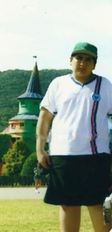 Guilherme na adolescência, de uniforme escolar e boné verde